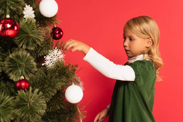 Girl in green dress decorating christmas tree isolated on red — Stock Photo