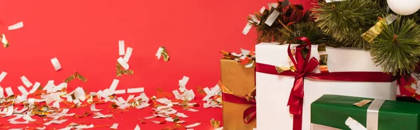 Cajas de regalo multicolores cerca del árbol de Navidad y confeti sobre fondo rojo, pancarta - foto de stock