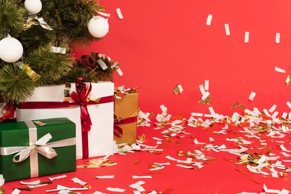 Presents under decorated christmas tree near falling confetti on red — Stock Photo