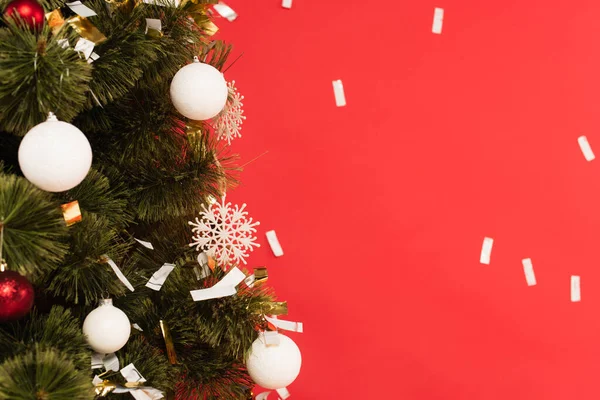 Vue rapprochée de l'arbre de Noël décoré près de confettis tombant isolé sur rouge — Photo de stock