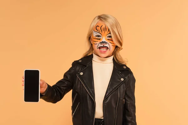 Дитина з малюнком обличчя тигра, що показує смартфон із порожнім екраном та гойданням ізольовано на бежевому — стокове фото