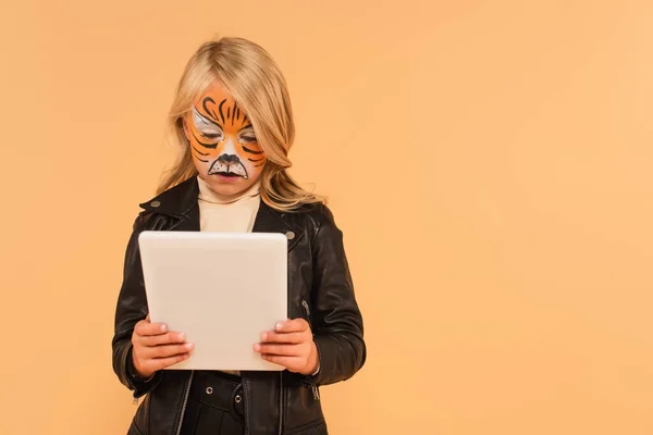 Niña con pintura facial de tigre utilizando tableta digital aislada en beige - foto de stock
