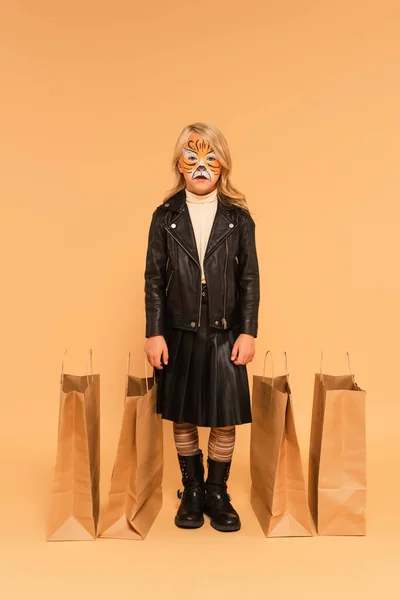 Повнометражний вид дівчини в тигровому макіяжі і стильний одяг біля сумки для покупок на бежевому — стокове фото
