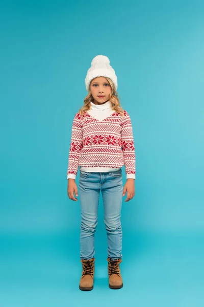 Full length view of child in warm hat, jeans and sweater with ornament on blue — Stock Photo