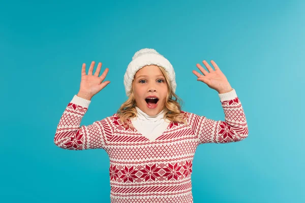 Menina animado em chapéu quente e suéter mostrando wow gesto isolado em azul — Fotografia de Stock