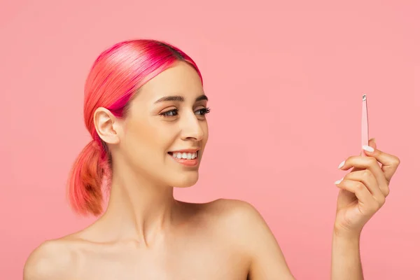 Allegra giovane donna con i capelli colorati guardando pinzette isolate su rosa — Foto stock