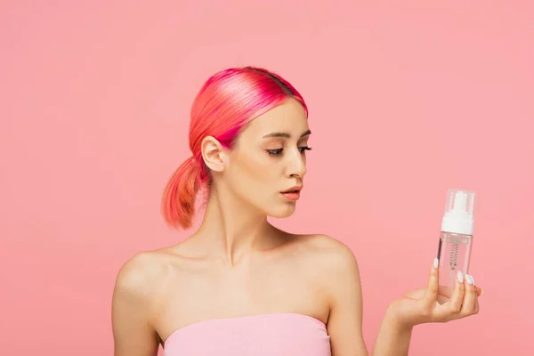 Jeune femme aux cheveux colorés regardant bouteille avec toner isolé sur rose — Photo de stock