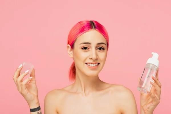 Jovem tatuada e feliz com garrafa de cabelo colorido segurando com toner isolado em rosa — Fotografia de Stock