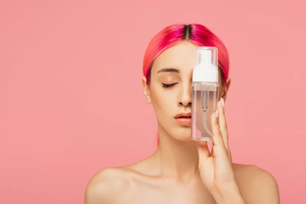 Young woman with dyed hair and closed eyes holding bottle with cleansing product isolated on pink — Stock Photo