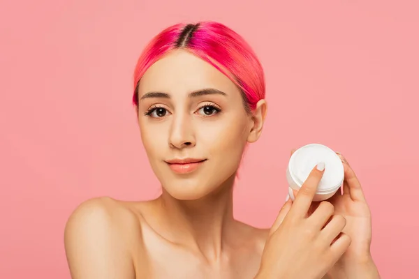 Jovem alegre com cabelo tingido segurando recipiente com creme cosmético isolado em rosa — Fotografia de Stock