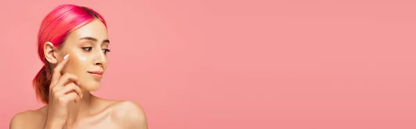 Young woman with colorful hair applying face cream isolated on pink, banner — Stock Photo