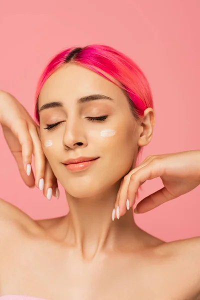 Mujer joven positiva con pelo colorido y crema facial en las mejillas aisladas en rosa - foto de stock