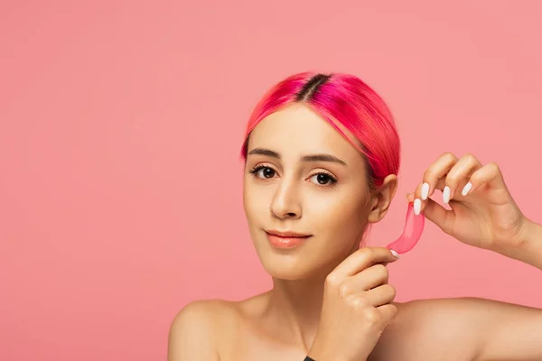 Positive junge Frau mit bunten Haaren hält feuchtigkeitsspendende Augenklappe isoliert auf rosa — Stockfoto