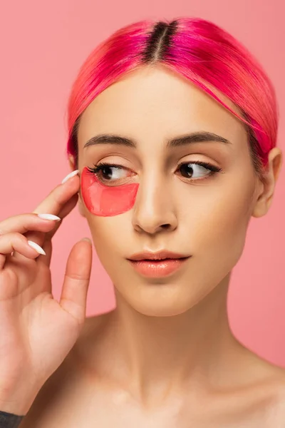Jeune femme aux cheveux colorés appliquant patch hydratant pour les yeux isolé sur rose — Photo de stock