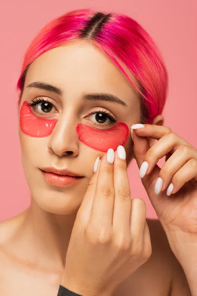 Bella giovane donna con i capelli colorati applicando toppe oculari di collagene isolato su rosa — Foto stock