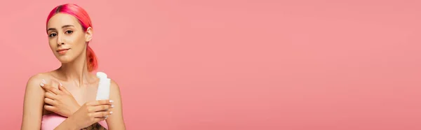 Jovem mulher com tubo de retenção de cabelo colorido ao aplicar o produto cosmético no ombro nu isolado em rosa, banner — Fotografia de Stock