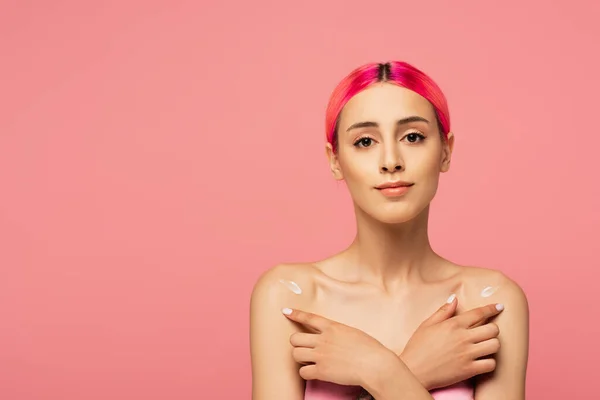 Mujer joven con pelo colorido aplicando loción sobre hombros desnudos aislados en rosa - foto de stock