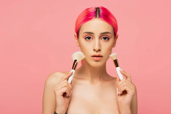 Young woman with colorful hair holding cosmetic brushes isolated on pink — Stock Photo