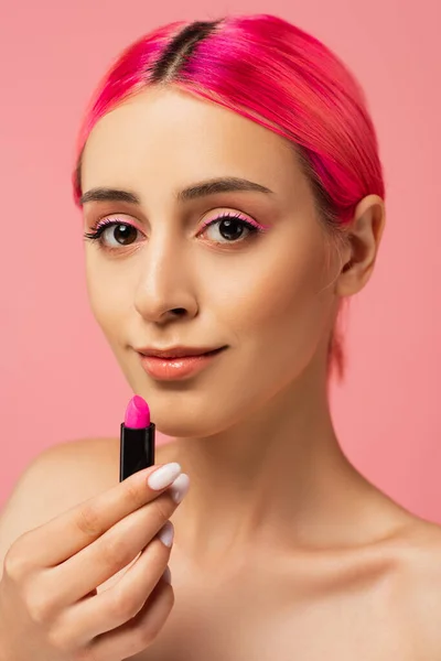 Heureux jeune femme avec des cheveux colorés tenant rouge à lèvres lumineux isolé sur rose — Photo de stock