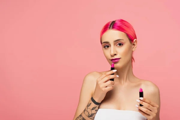Young woman with colorful hair holding lipsticks isolated on pink — Stock Photo