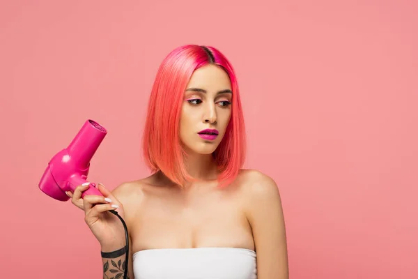 Татуйована молода жінка з барвистим волоссям, що тримає фен ізольовані на рожевому — стокове фото