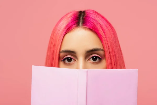 Giovane donna con i capelli colorati che coprono il viso con libro isolato su rosa — Foto stock