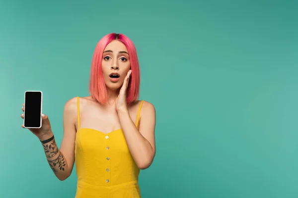 Shocked young woman with pink dyed hair holding smartphone with blank screen isolated on turquoise — Stock Photo