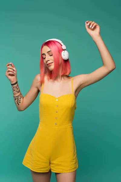 Mujer joven con el pelo teñido de rosa escuchando música en los auriculares y bailando aislado en azul - foto de stock
