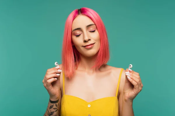 Mulher jovem satisfeito com cabelo tingido rosa segurando fones de ouvido sem fio isolados em azul — Fotografia de Stock