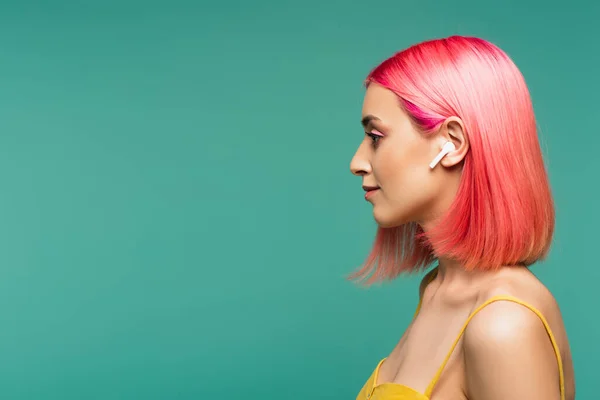 Vista lateral de mujer joven con cabello teñido de rosa en auriculares inalámbricos aislados en azul - foto de stock