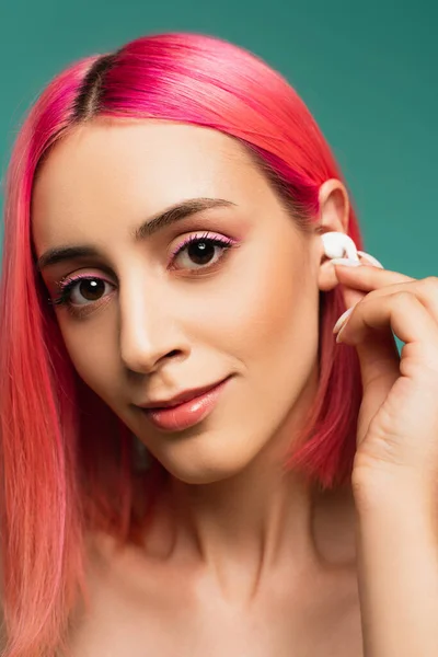 Giovane donna con capelli rosa tinti regolazione auricolare wireless isolato su blu — Foto stock