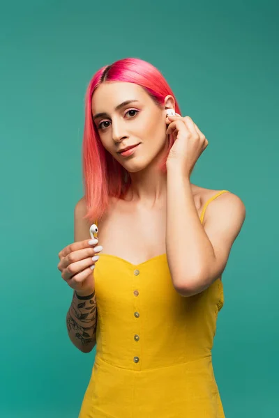 Hübsche junge Frau mit rosa gefärbten Haaren, die drahtlose Kopfhörer isoliert auf blau hält — Stockfoto