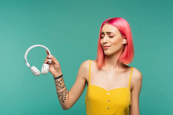 Скептична молода жінка в навушниках тримає бездротові навушники ізольовані на синьому — стокове фото
