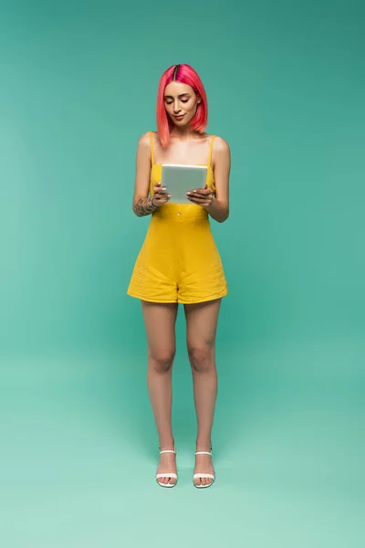 Volle Länge der jungen Frau mit rosa gefärbten Haaren hält digitale Tablette auf blau — Stockfoto