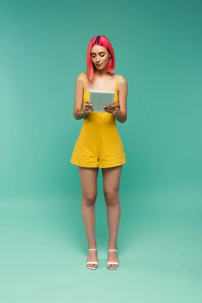 Comprimento total da jovem mulher com cabelo tingido rosa segurando tablet digital em azul — Fotografia de Stock