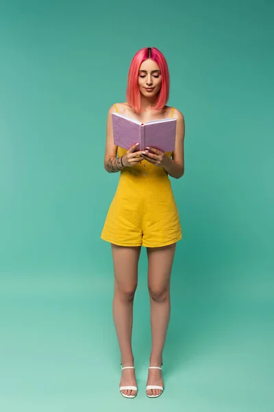 Повнометражна молода жінка з рожевим фарбованим волоссям читає книгу на синьому — стокове фото