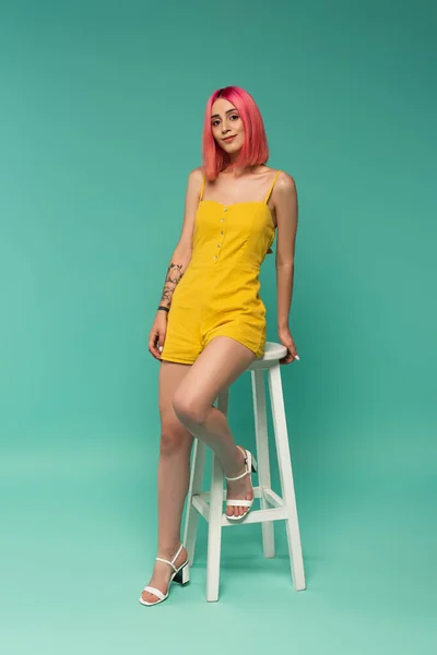 Full length of happy young woman with pink dyed hair sitting on stool on blue — Stock Photo