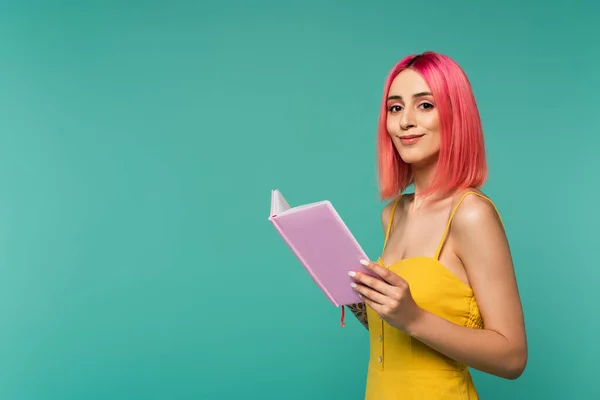 Happy young woman with pink dyed hair holding book isolated on blue — Stock Photo