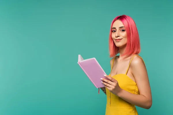 Heureux jeune femme avec rose teint cheveux tenant livre isolé sur bleu — Photo de stock