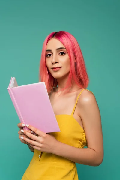 Jolie jeune femme avec des cheveux teints en rose tenant livre isolé sur bleu — Photo de stock