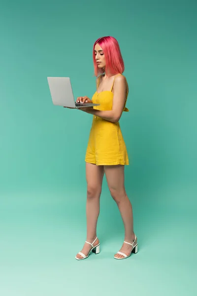 Pleine longueur de jeune femme avec des cheveux teints en rose à l'aide d'un ordinateur portable sur bleu — Photo de stock