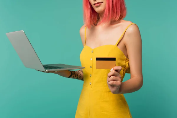 Vista cortada de mulher jovem com cabelo tingido rosa segurando cartão de crédito e laptop isolado em azul — Fotografia de Stock