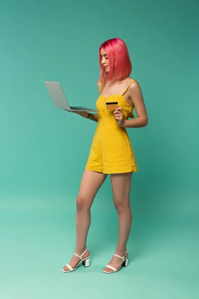 Piena lunghezza della giovane donna con capelli rosa tinti con carta di credito e laptop su blu — Foto stock
