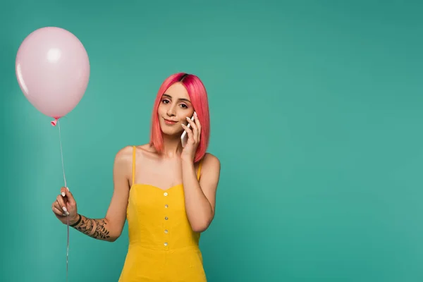 Junge Frau mit rosa gefärbten Haaren hält Luftballon und telefoniert isoliert auf blauem Grund — Stockfoto