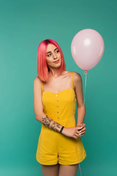 Curiosa joven con el pelo teñido de rosa mirando globo aislado en azul - foto de stock