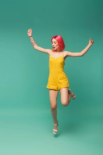 Full length of excited young woman with pink dyed hair in romper jumping on blue — Stock Photo
