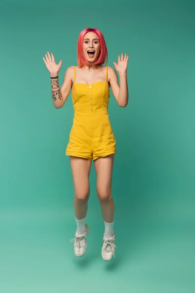 Full length of excited young woman with pink dyed hair jumping on blue — Stock Photo