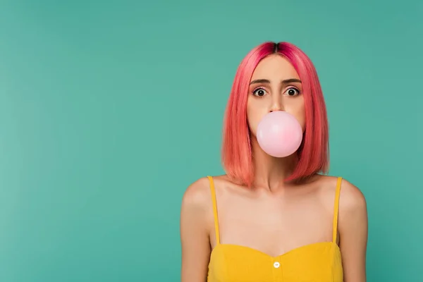Mujer joven con el pelo teñido rosa que sopla goma de mascar aislada en azul - foto de stock