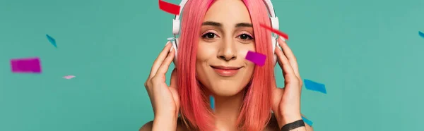 Happy young woman with pink dyed hair in wireless headphones near colorful confetti on blue, banner — Stock Photo