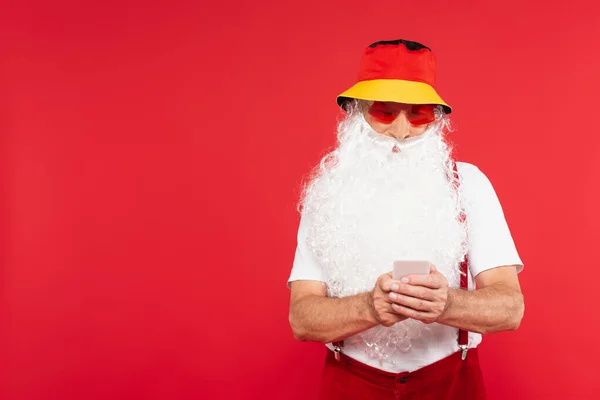 Santa Claus en panama y gafas de sol usando celular aislado en rojo - foto de stock